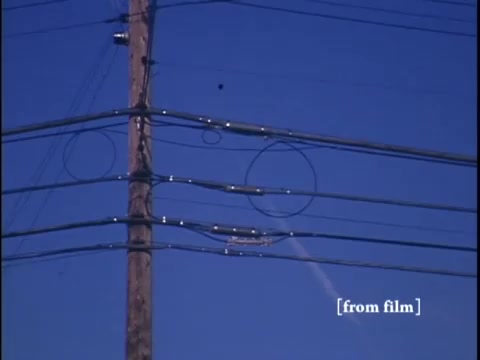 Upward perspective of urban infrastructure and power lines against a clear blue sky.